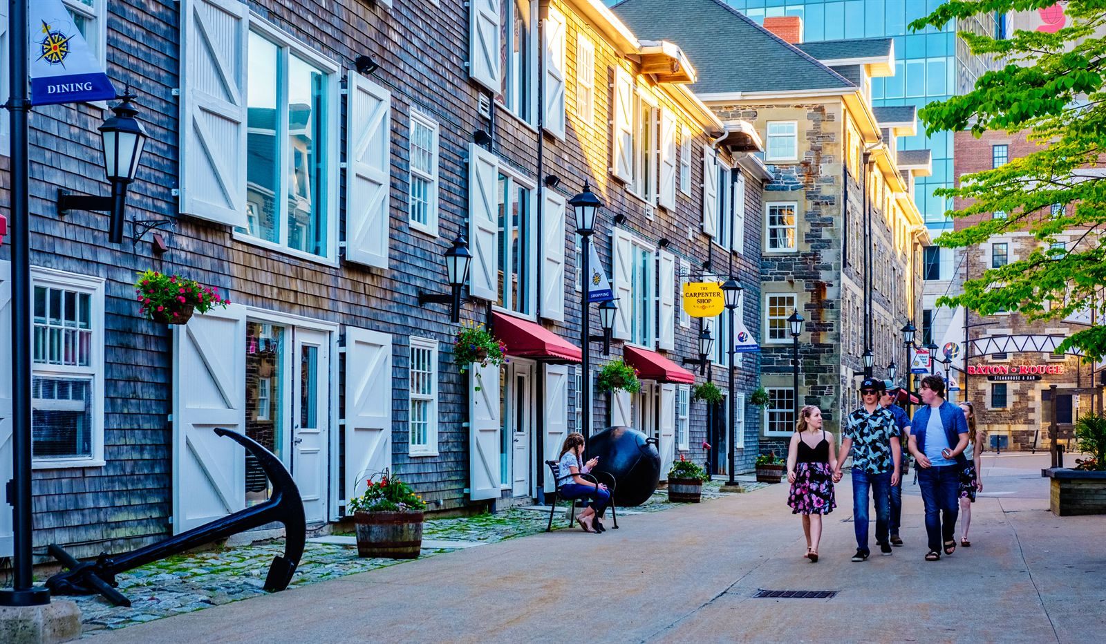Pedestrians on a lane of shingled historic buildings with an old anchor on display, Halifax waterfront