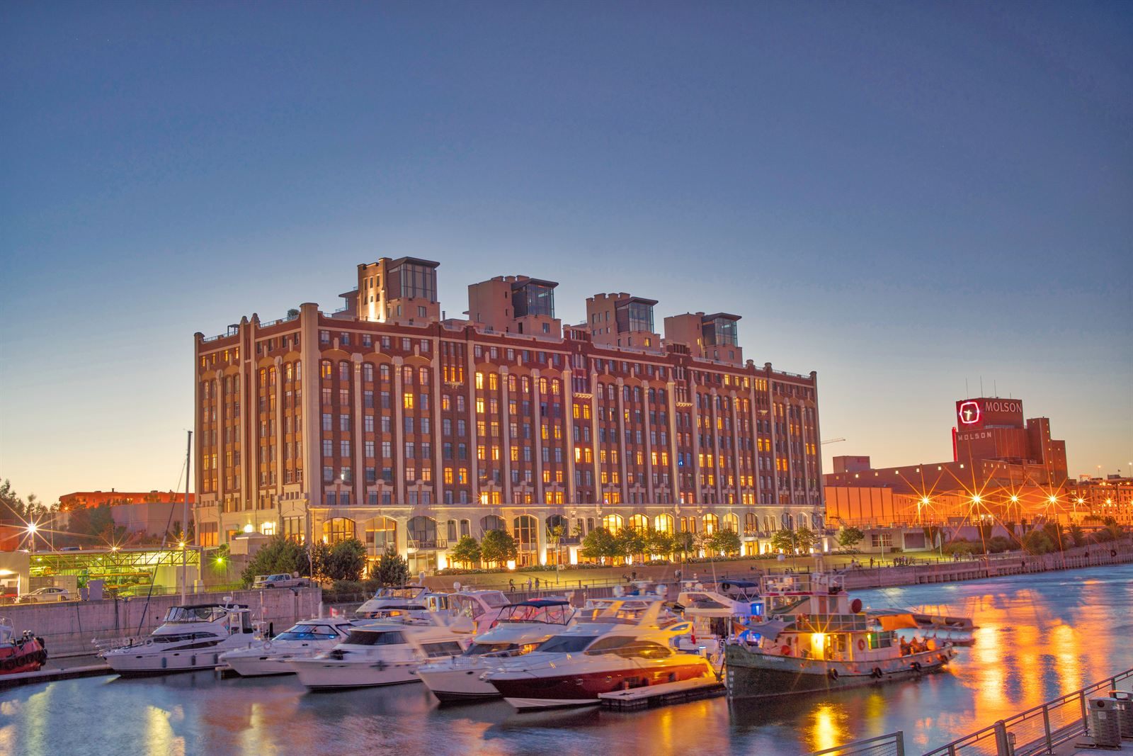 Motor yachts moored at a marina in the Old Port of Montreal in front of a large brick building at dusk