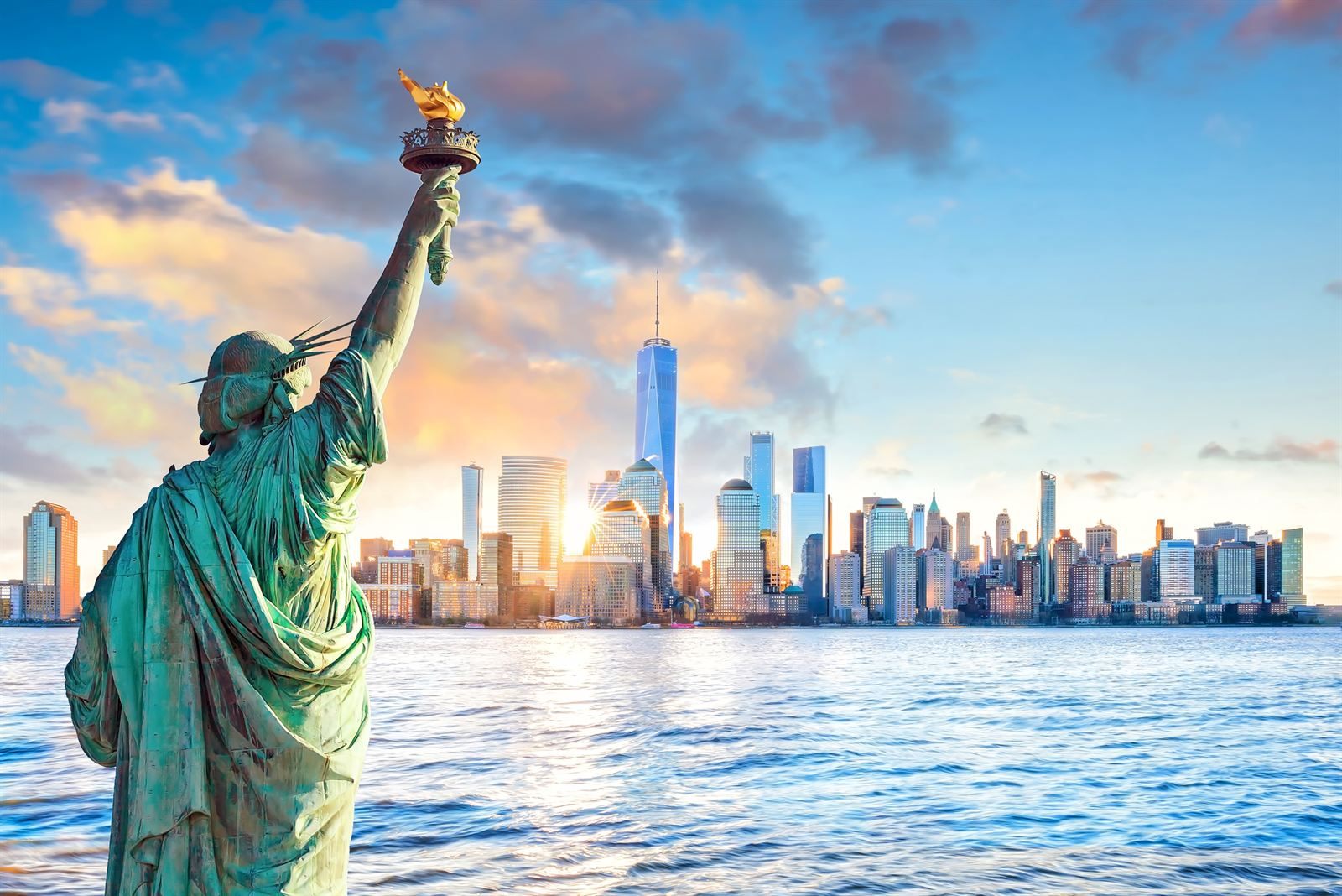 The Statue of Liberty's raised torch with the Lower Manhattan skyline across the harbor at sunset