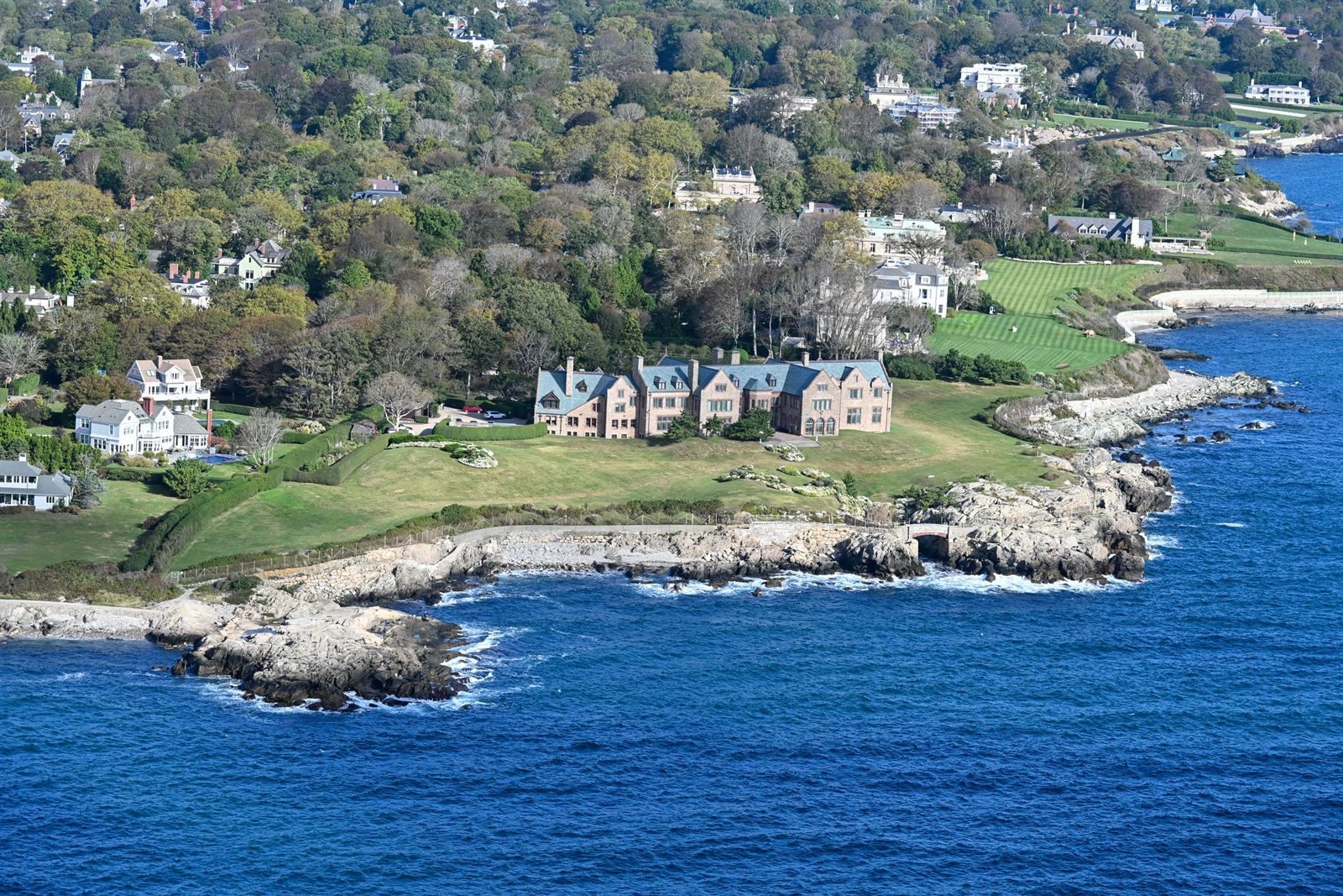 Aerial view of a large stone mansion and lawns on a rocky ocean point in Newport, Rhode Island